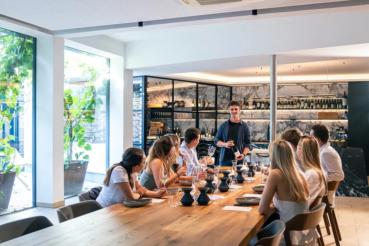 Eine Gruppe von Gästen bei einer Weinverkostung an einem langen Holztisch.